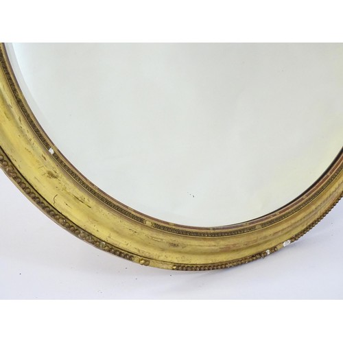 1658 - A 19thC oval giltwood and gesso wall mirror with bevelled glass. The surround having moulded and bea... 