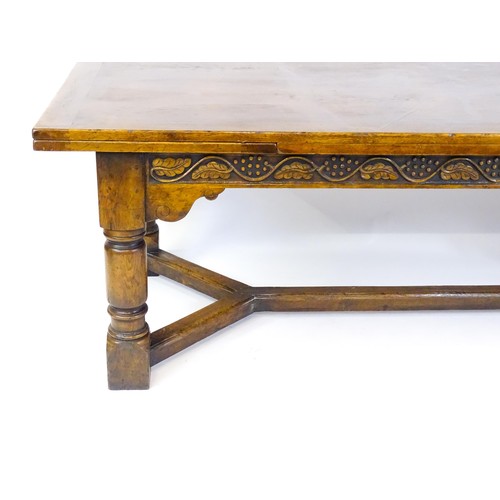 1684 - An early 20thC oak dining table with draw leaves to each end,  carved frieze with grapes and fruitin... 