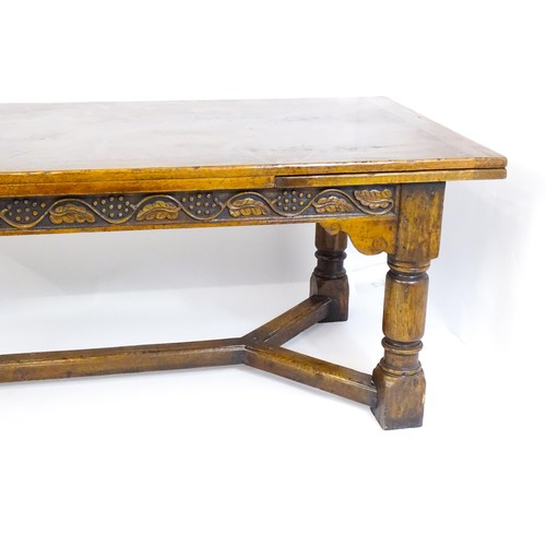 1684 - An early 20thC oak dining table with draw leaves to each end,  carved frieze with grapes and fruitin... 