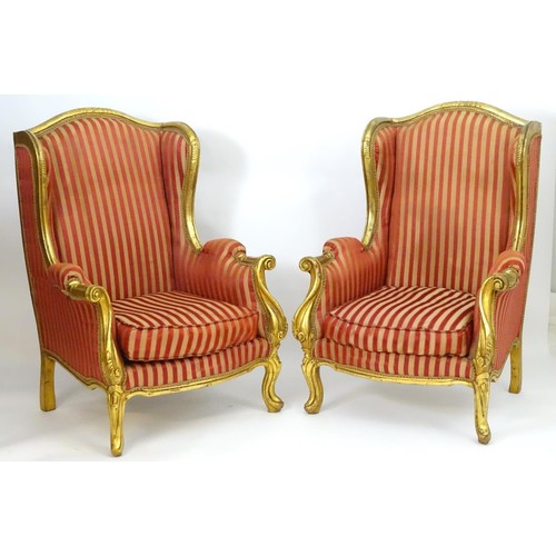 1732 - A pair of mid 20thC large gilt wingback armchairs, having moulded frames with floral decoration, scr... 