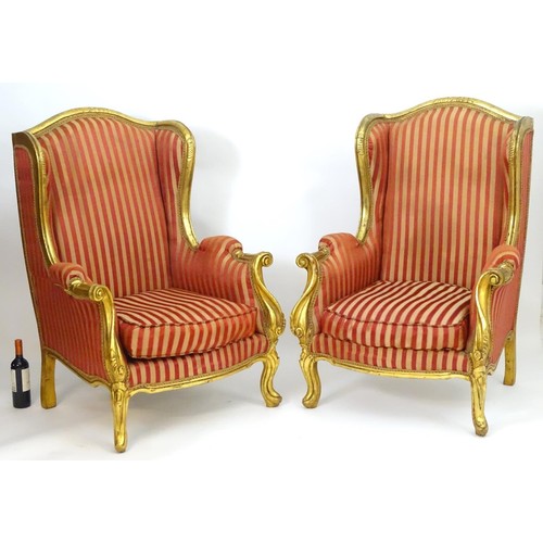 1732 - A pair of mid 20thC large gilt wingback armchairs, having moulded frames with floral decoration, scr... 