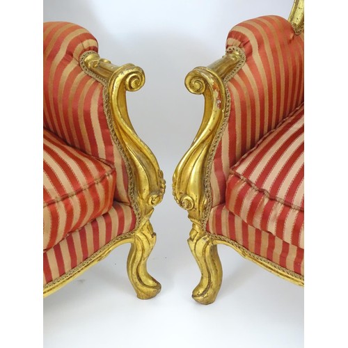 1732 - A pair of mid 20thC large gilt wingback armchairs, having moulded frames with floral decoration, scr... 