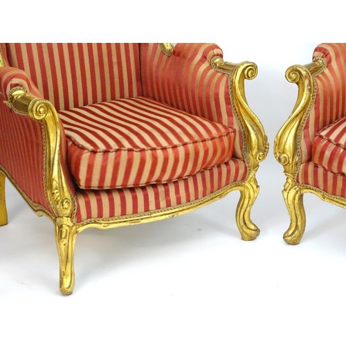 1732 - A pair of mid 20thC large gilt wingback armchairs, having moulded frames with floral decoration, scr... 