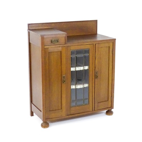 1736 - An Arts & Crafts oak cabinet with an upstand above a single short drawer and two panelled doors and ... 