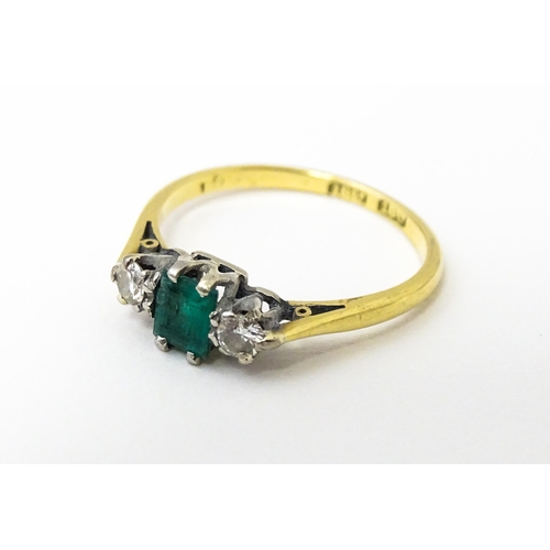 631 - An 18ct gold ring set with central emerald flanked by diamonds. Ring size approx. L