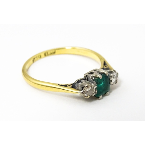 631 - An 18ct gold ring set with central emerald flanked by diamonds. Ring size approx. L