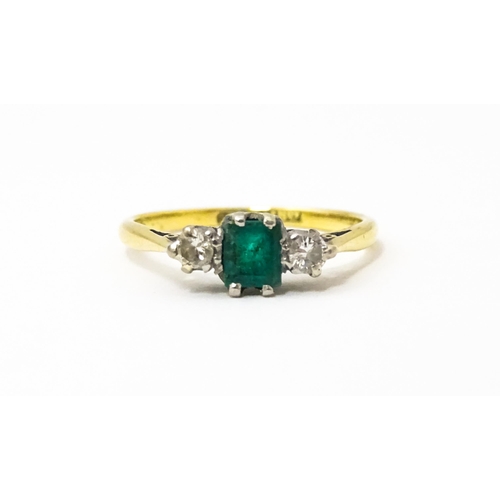 631 - An 18ct gold ring set with central emerald flanked by diamonds. Ring size approx. L