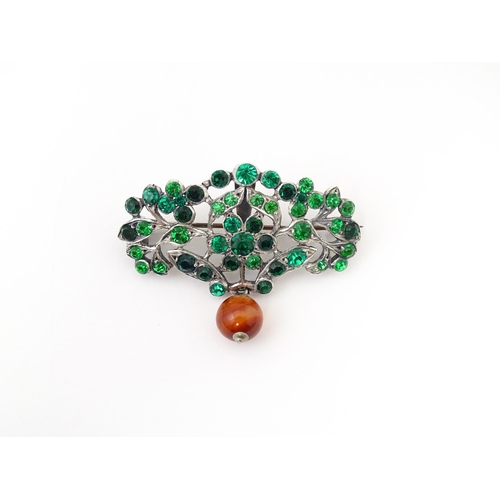 673 - A white metal brooch set with green paste stones and carnelian bead drop. Approx 2