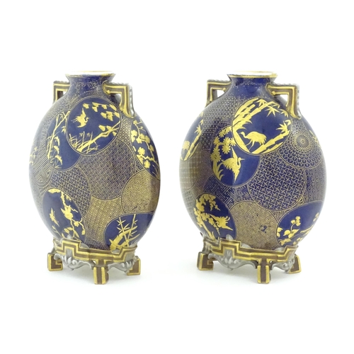 112 - Two Royal Worcester Aesthetic Movement moon flask vases with twin gilt handles and raised feet, the ... 