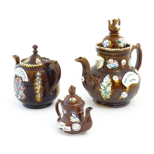 122 - Three Victorian treacle glazed bargeware teapots. with applied flower and banner detail. The largest... 