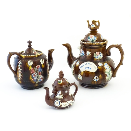 122 - Three Victorian treacle glazed bargeware teapots. with applied flower and banner detail. The largest... 