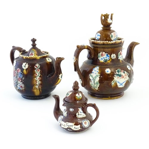 122 - Three Victorian treacle glazed bargeware teapots. with applied flower and banner detail. The largest... 