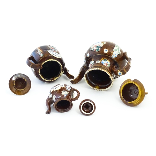 122 - Three Victorian treacle glazed bargeware teapots. with applied flower and banner detail. The largest... 