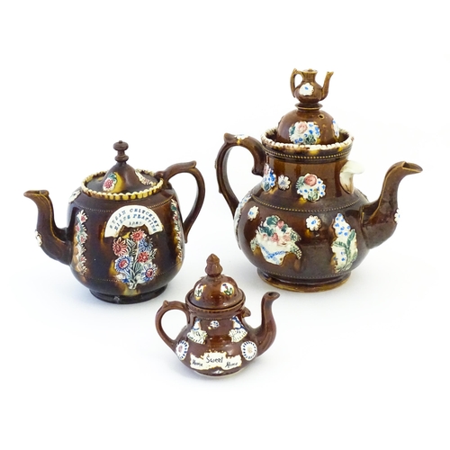 122 - Three Victorian treacle glazed bargeware teapots. with applied flower and banner detail. The largest... 