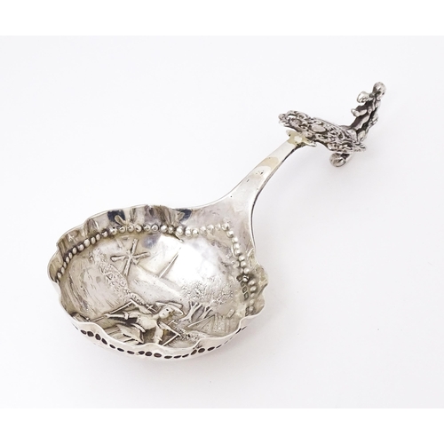 390 - A Dutch silver caddy spoon with landscape scene with figure, windmill etc to bowl and scroll, figure... 