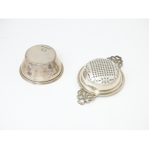 471 - A silver twin handled lemon / tea strainer with pierced detail and bowl under. Hallmarked Birmingham... 