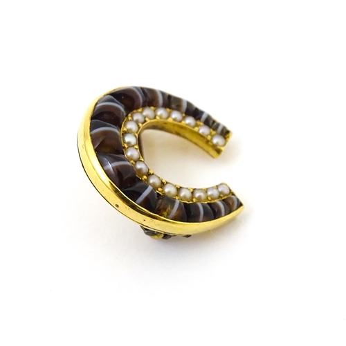 686 - A yellow metal brooch of horseshoe form set with cats eye cabochon and seed pearls. 3 3/4