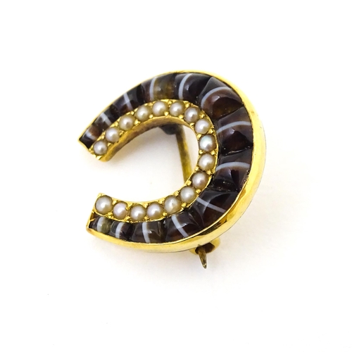 686 - A yellow metal brooch of horseshoe form set with cats eye cabochon and seed pearls. 3 3/4