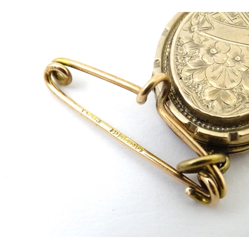 695 - A yellow metal pendant locket with engraved decoration suspended from a 9ct gold brooch hanger hallm... 