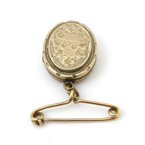 695 - A yellow metal pendant locket with engraved decoration suspended from a 9ct gold brooch hanger hallm... 