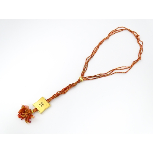 709 - A necklace of twisted orange and golden coloured thread form with gilt metal sliders and pendant mar... 