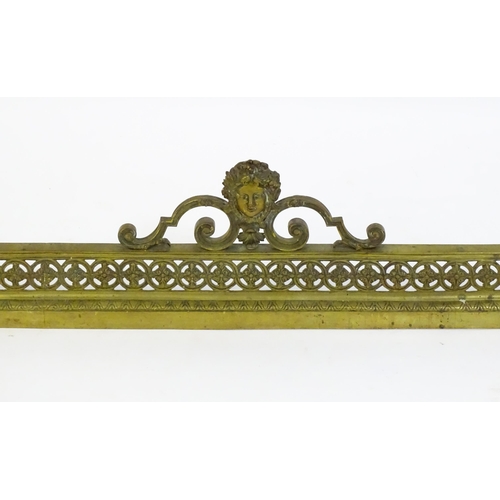 1367 - A late 19thC brass fender with a pierced, moulded frame and a female mask flanked by scrolled tendri... 