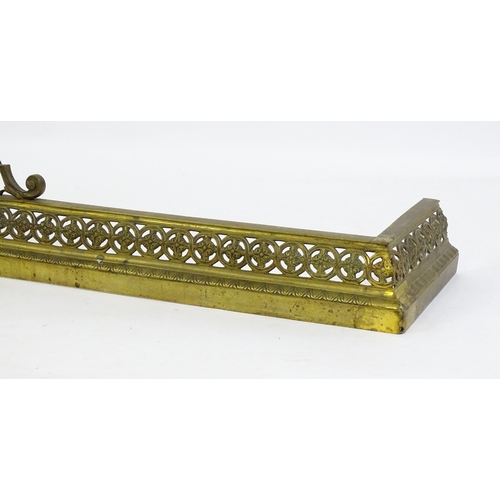 1367 - A late 19thC brass fender with a pierced, moulded frame and a female mask flanked by scrolled tendri... 