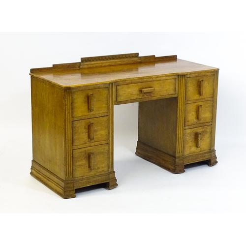 1621 - An Art Deco oak desk / dressing table with a shaped upstand, inverted breakfront top and fluted pila... 