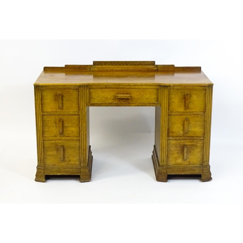 1621 - An Art Deco oak desk / dressing table with a shaped upstand, inverted breakfront top and fluted pila... 