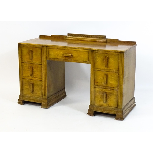 1621 - An Art Deco oak desk / dressing table with a shaped upstand, inverted breakfront top and fluted pila... 