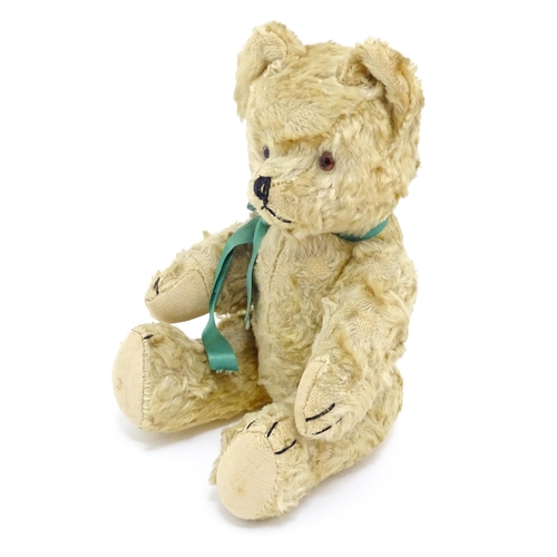 1437 - Toy: A 20thC plush teddy bear with stitched nose, mouth and claws, pad paws and a green ribbon. Appr... 