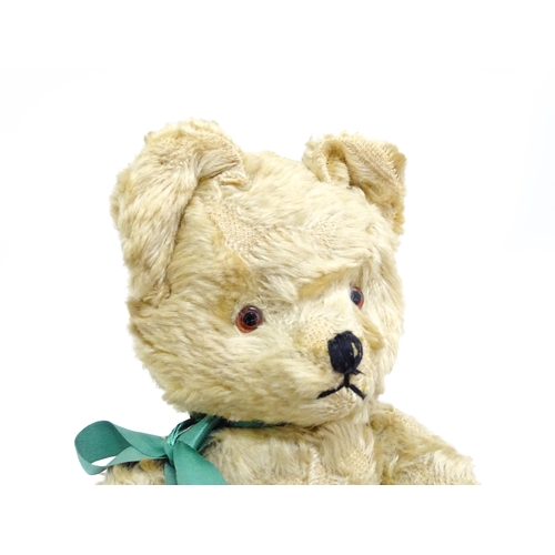 1437 - Toy: A 20thC plush teddy bear with stitched nose, mouth and claws, pad paws and a green ribbon. Appr... 