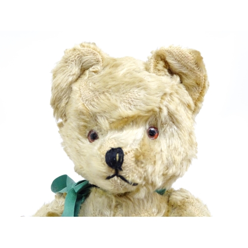 1437 - Toy: A 20thC plush teddy bear with stitched nose, mouth and claws, pad paws and a green ribbon. Appr... 