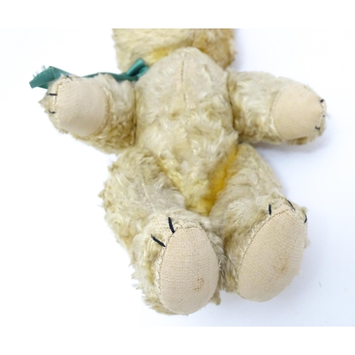 1437 - Toy: A 20thC plush teddy bear with stitched nose, mouth and claws, pad paws and a green ribbon. Appr... 