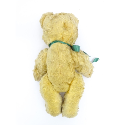 1437 - Toy: A 20thC plush teddy bear with stitched nose, mouth and claws, pad paws and a green ribbon. Appr... 