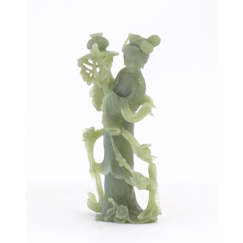 1123 - An Oriental jade coloured hardstone carving modelled as a woman with flowing drapery and flowers hol... 