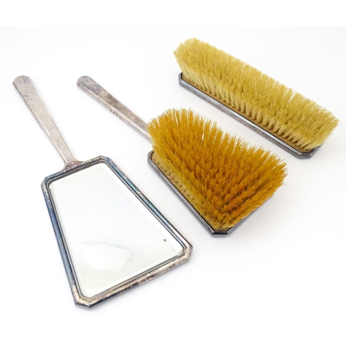 584 - A cased Art Deco dressing table set comprising two silver handled brushes and hand mirror with engin... 