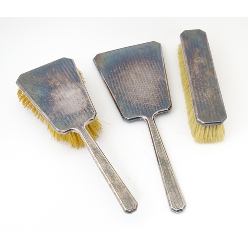 584 - A cased Art Deco dressing table set comprising two silver handled brushes and hand mirror with engin... 