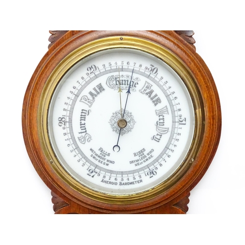 1550 - A 20thC aneroid barometer surmounted by thermometer within a carved wooden surround.  Approx. 30