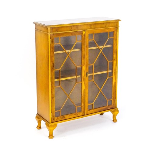 36 - A yew wood veneered astragal glazed cabinet with a moulded top and two doors and raised on four cabr... 