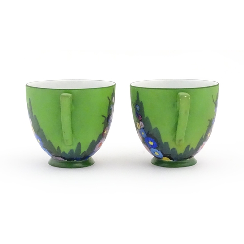 78 - Two Art Deco cups and saucers with a green ground and hollyhock flower decoration. Marked Carlton un... 