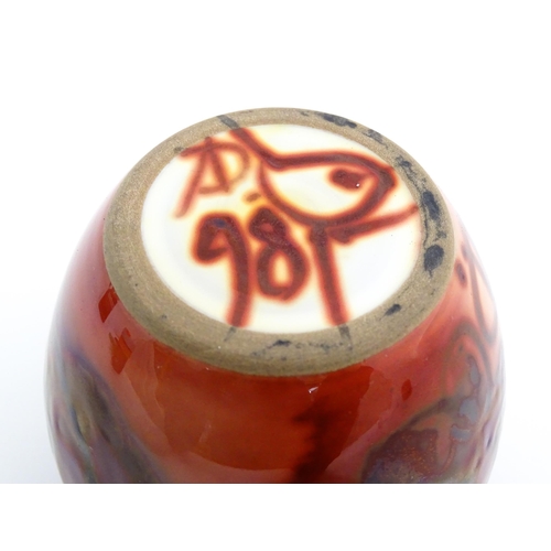 88 - A studio pottery vase with a red ground and lustre detail. Signed under with monogram AD, bird motif... 