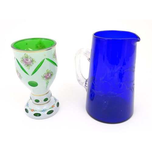 219 - A Bohemian glass goblet with green glass detail and floral decoration together with a blue glass jug... 