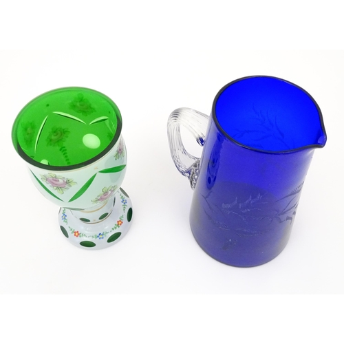 219 - A Bohemian glass goblet with green glass detail and floral decoration together with a blue glass jug... 