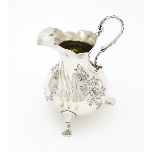 268 - A Victorian silver cream jug with engraved decoration raised on three swept feet, hallmarked London ... 