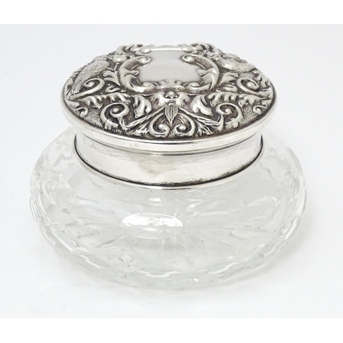 295 - A cut glass powder pot with silver lid having embossed decoration and mirror under. Hallmarked Birmi... 