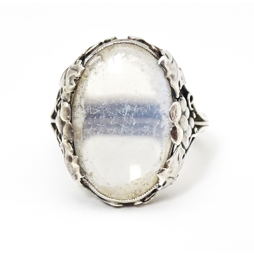 640 - A white metal ring set with central oval moonstone cabochon and with fruiting vine detail to shoulde... 