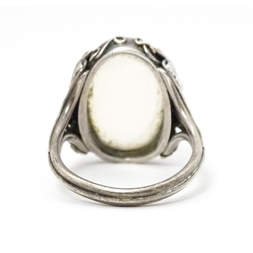 640 - A white metal ring set with central oval moonstone cabochon and with fruiting vine detail to shoulde... 