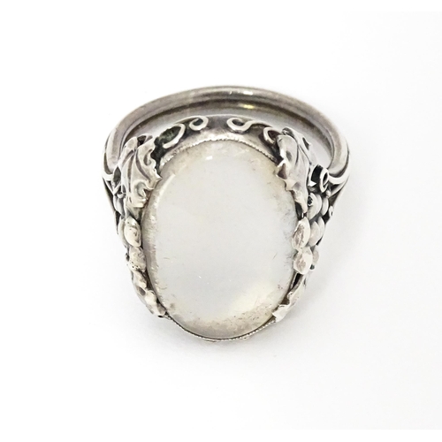 640 - A white metal ring set with central oval moonstone cabochon and with fruiting vine detail to shoulde... 