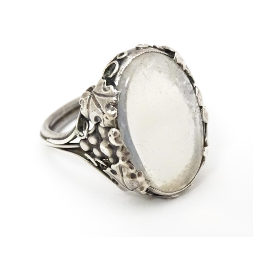 640 - A white metal ring set with central oval moonstone cabochon and with fruiting vine detail to shoulde... 